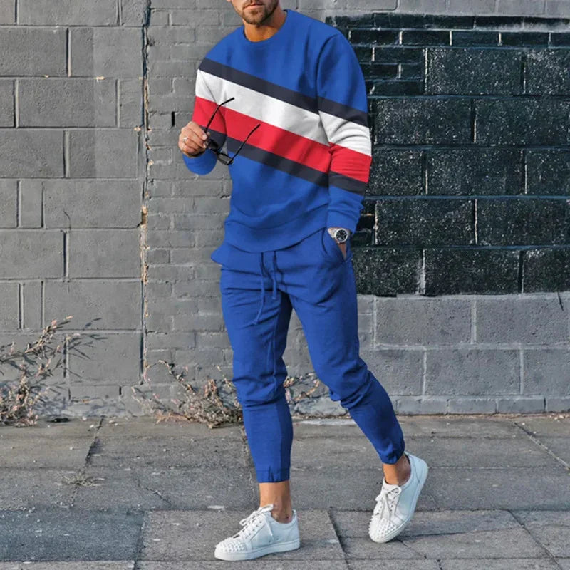 Man wearing blue jogger set with red, white, and black stripe sweatshirt and white sneakers against urban brick wall