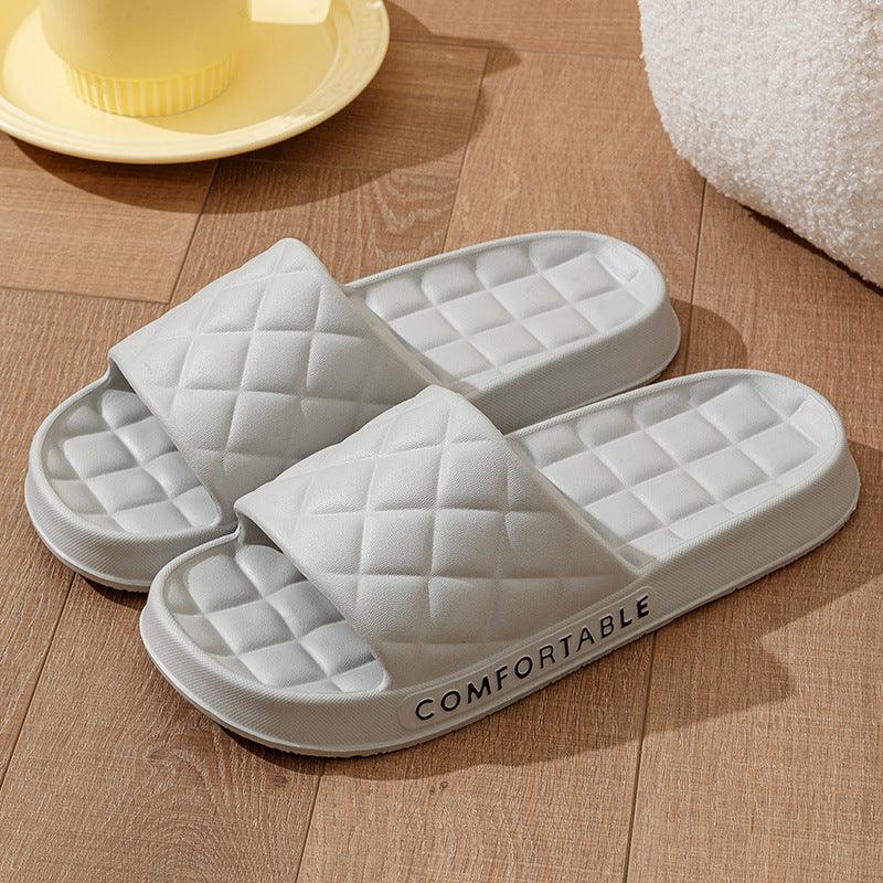 White quilted slide slippers on wooden floor with 'COMFORTABLE' text on side, cozy home footwear