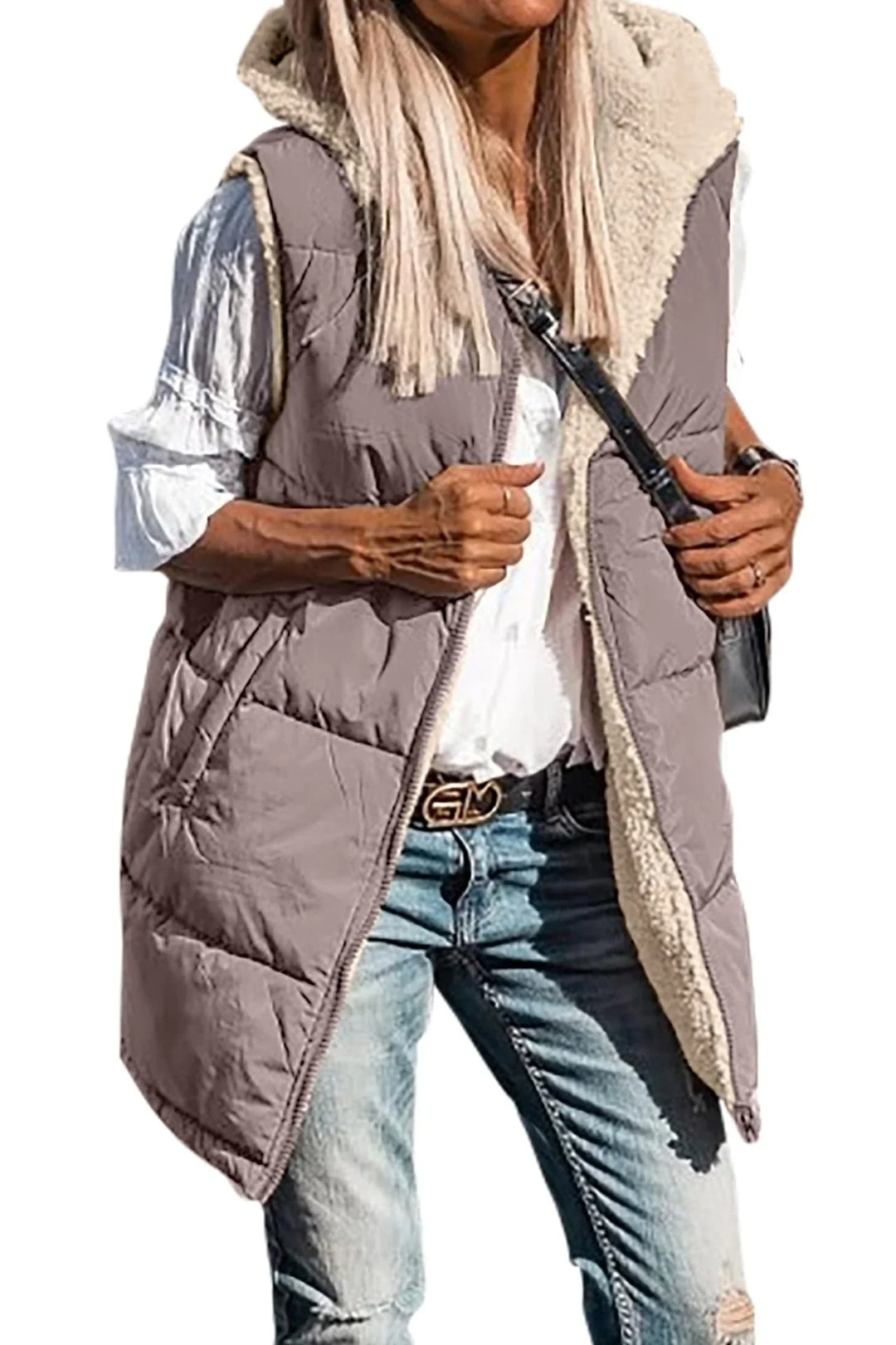 Woman wearing hooded sleeveless quilted vest with sherpa lining, white blouse, and distressed jeans