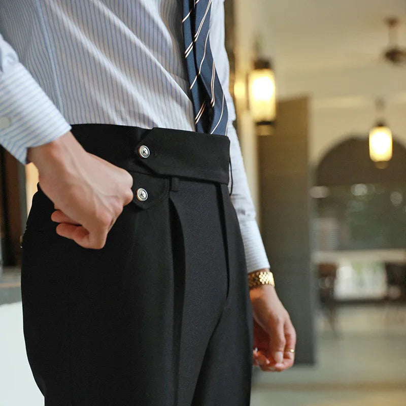 Close-up of man adjusting black high-waist dress pants with double button and pleats, wearing striped shirt and tie
