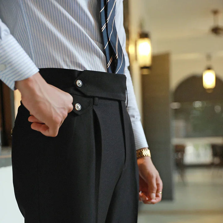 Close-up of man adjusting black high-waist dress pants with double button and pleats, wearing striped shirt and tie