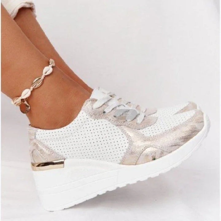 White perforated wedge sneakers with metallic gold accents worn with shell anklet