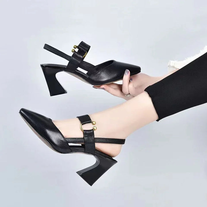 Black leather slingback heels with gold ball accents, worn with black pants against a plain background