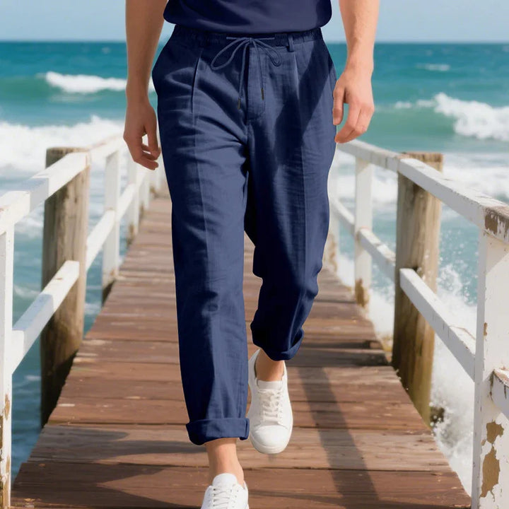 Man walking on wooden pier by ocean wearing navy blue casual pants and white sneakers