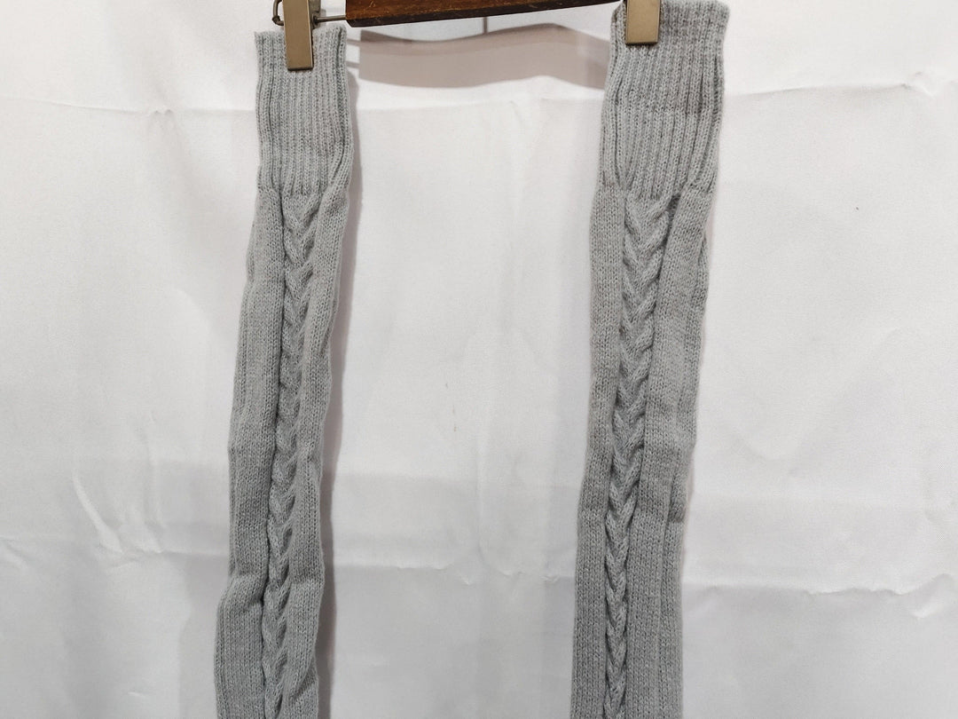 Gray knit leg warmers with cable pattern hanging on wooden hanger against white background