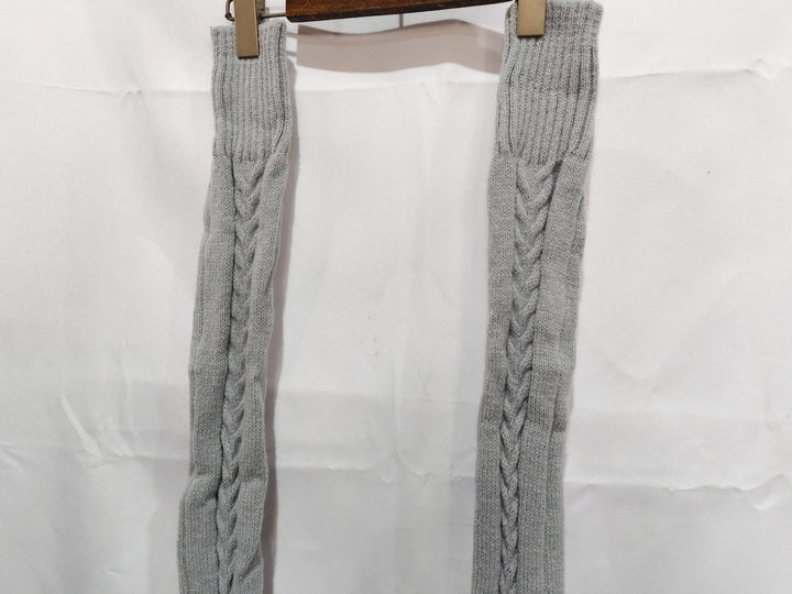 Gray knit leg warmers with cable pattern hanging on wooden hanger against white background