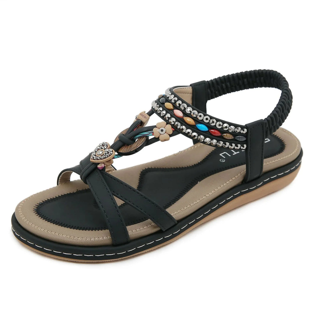 Black flat sandal with colorful beads, decorative heart and flower charms, and a tan cushioned sole