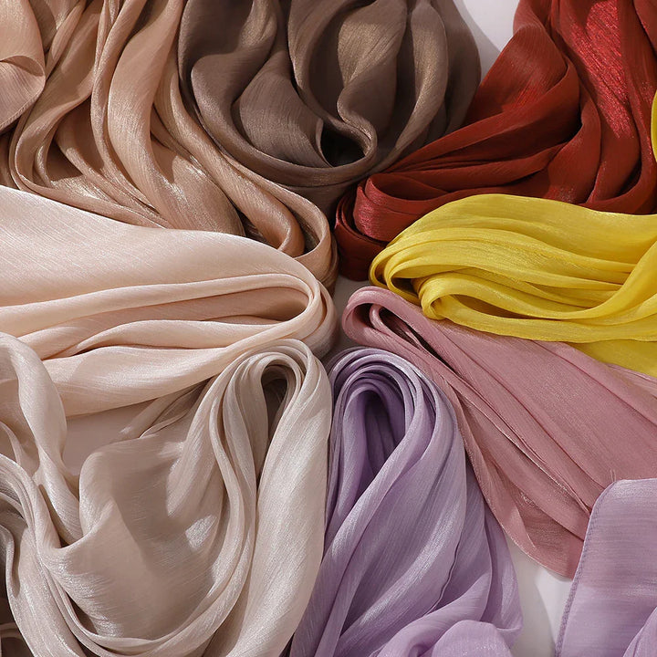 Assorted soft silk scarves in beige, brown, red, yellow, pink, and lavender shades arranged in folds