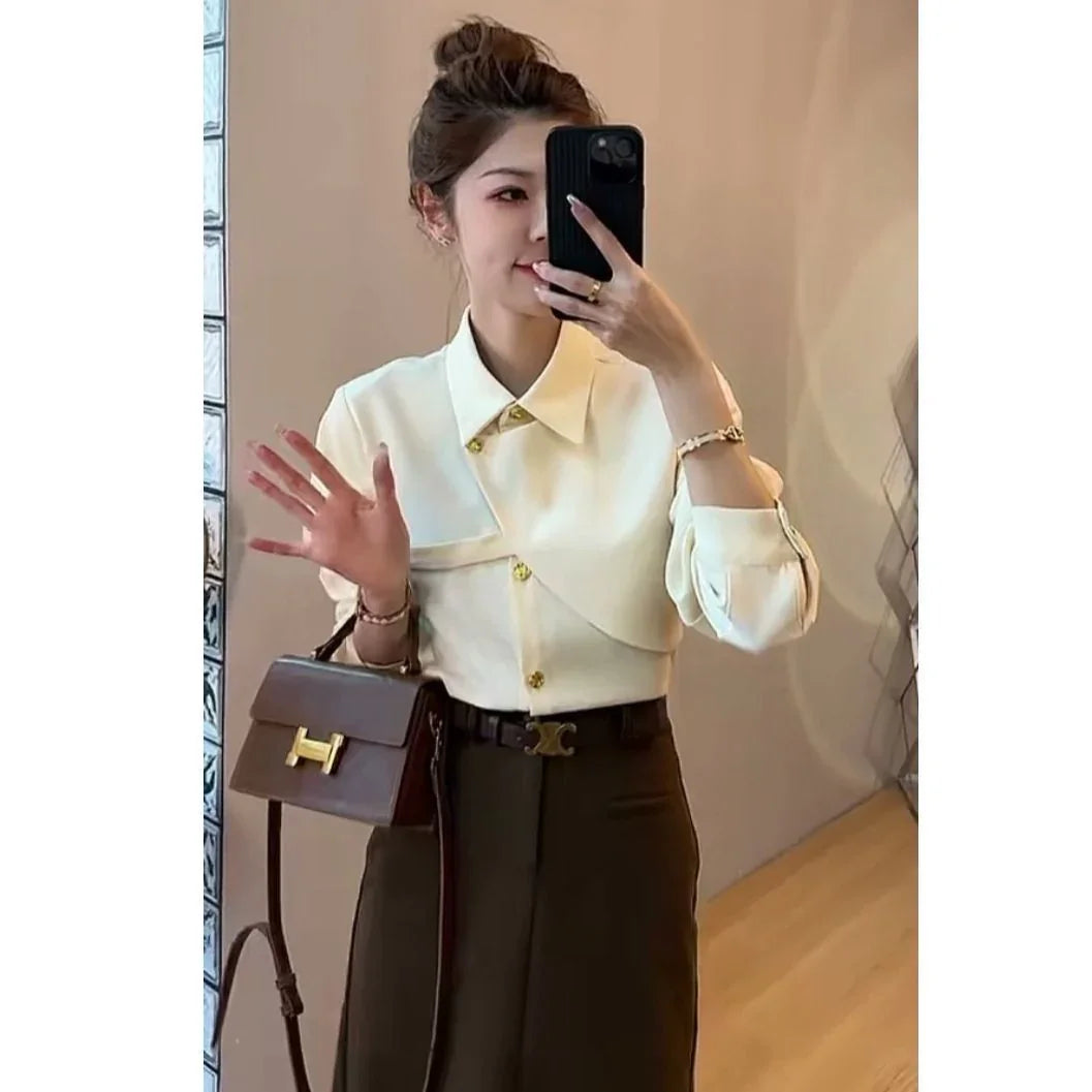 Woman taking mirror selfie wearing white asymmetrical blouse, dark skirt, and carrying brown handbag