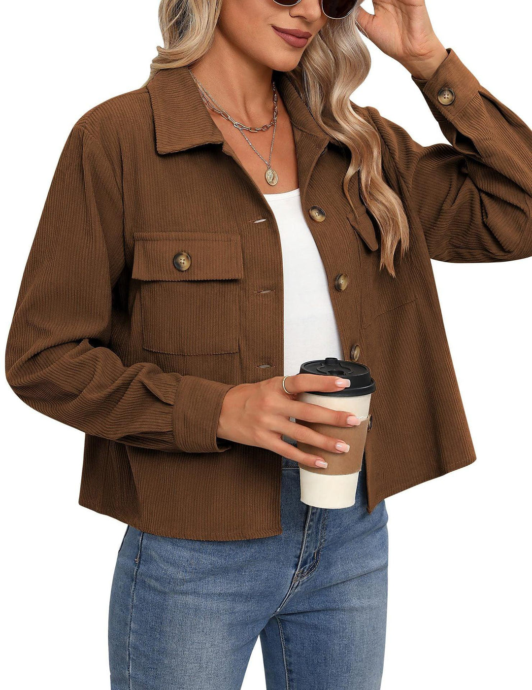 Woman wearing brown corduroy button-up jacket, white top, blue jeans holding coffee cup