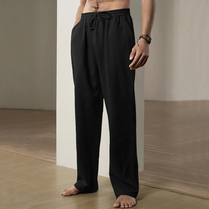 Barefoot man wearing black drawstring lounge pants standing indoors on wooden floor