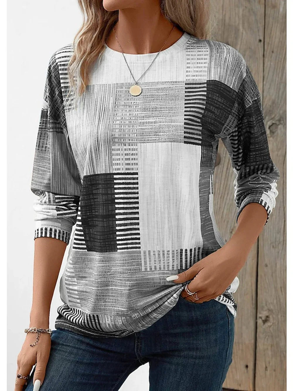 Woman wearing black and white patchwork long sleeve casual top with jeans and gold pendant necklace