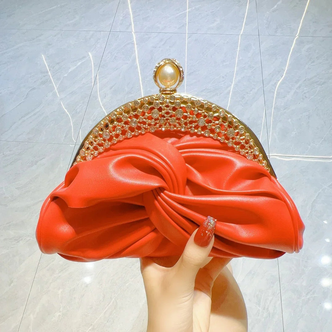 Red satin clutch purse with gold rhinestone frame and pearl clasp held by hand