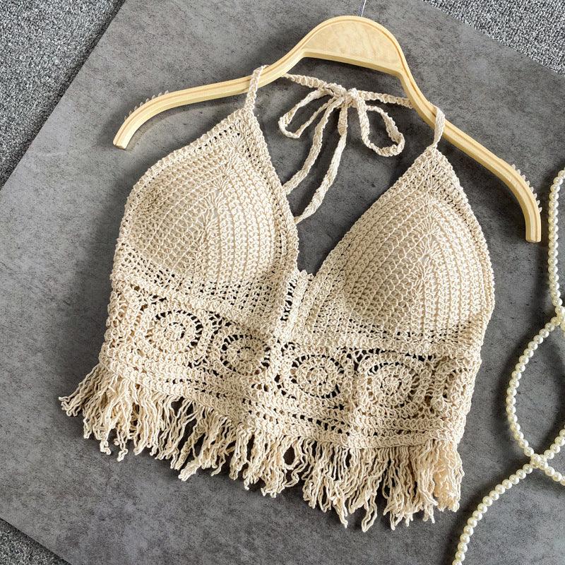 Beige crochet halter top with fringe detailing on wooden hanger on grey surface