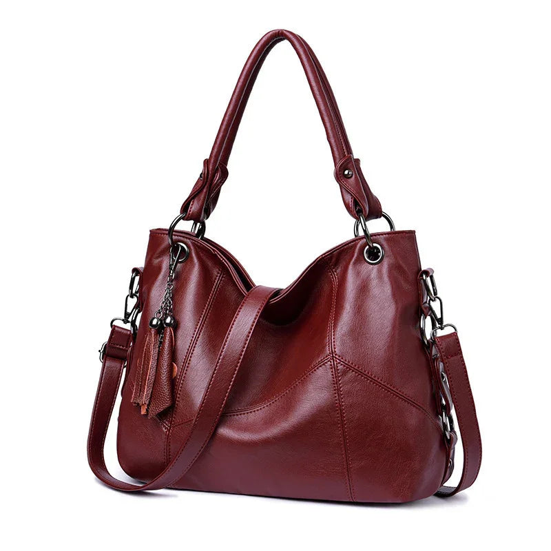 Elegant maroon leather handbag with dual handles, detachable shoulder strap, and tassel charms
