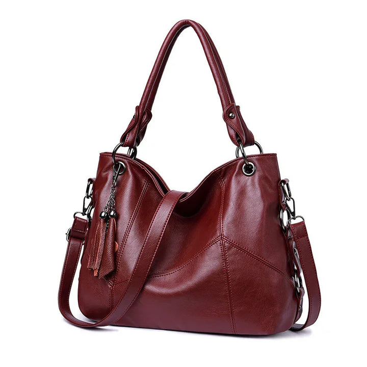 Elegant maroon leather handbag with dual handles, detachable shoulder strap, and tassel charms