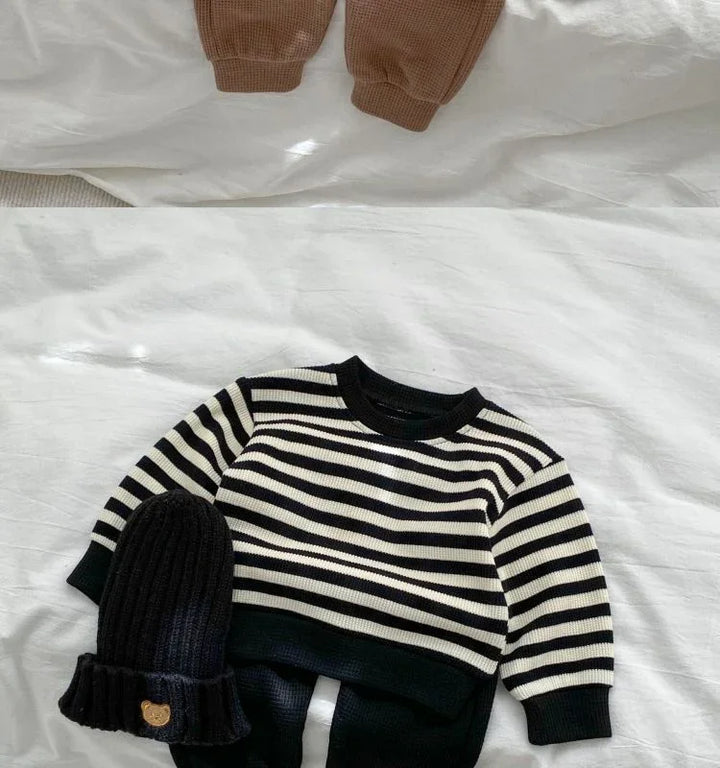 Black and white striped knit sweater paired with black knit beanie on white bedspread