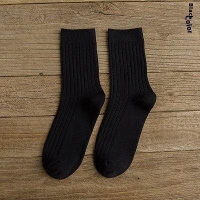 Pair of black ribbed socks laid flat on wooden surface with label 'Black color'