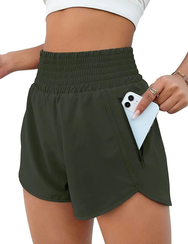 Close-up of woman wearing dark green high-waisted athletic shorts with zip pocket holding a white smartphone