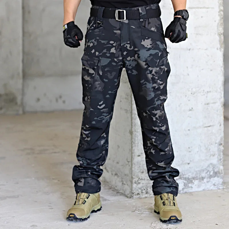 Man wearing black and gray camouflage tactical pants with black gloves and tan combat boots