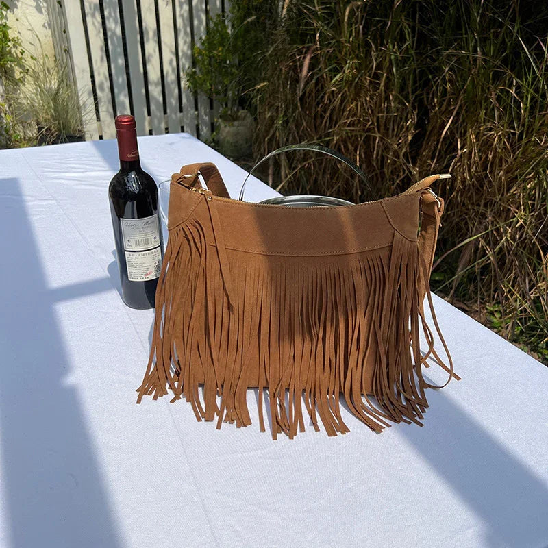 Brown suede fringe handbag and red wine bottle on white outdoor table with garden background