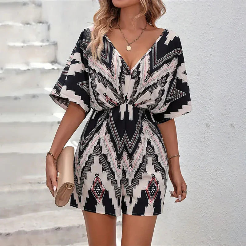 Woman wearing black and white geometric patterned short romper with V-neck and loose sleeves, holding beige clutch