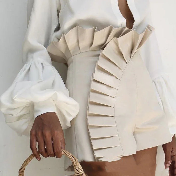 Close-up of a woman wearing high-waisted beige shorts with ruffle detailing and a white blouse with voluminous sleeves