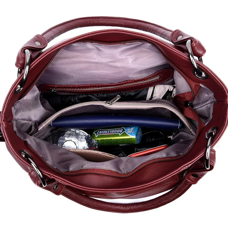 Open burgundy leather handbag showing organized interior with wallet, gum pack, water bottle, and zipped compartments