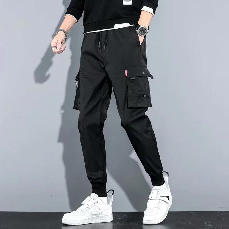 Man wearing black cargo jogger pants with side pockets and white sneakers against gray background