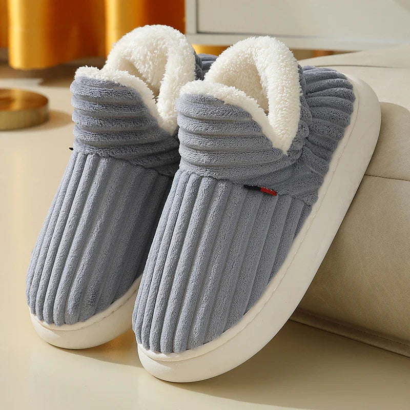 Gray ribbed indoor slippers with white plush lining and thick white soles on beige surface