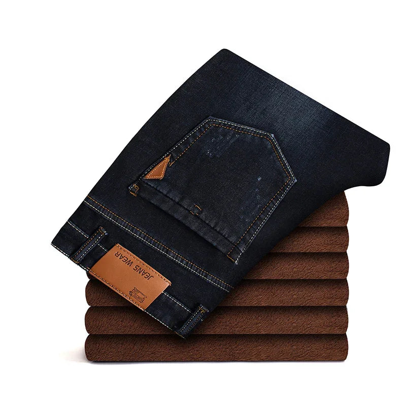 Folded black denim jeans with leather patches stacked on brown fabric