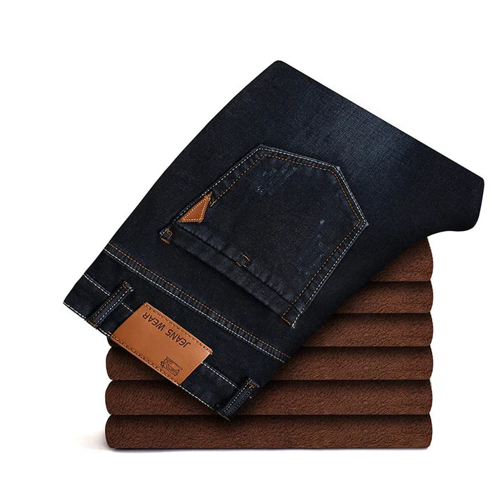 Folded black denim jeans with leather patches stacked on brown fabric