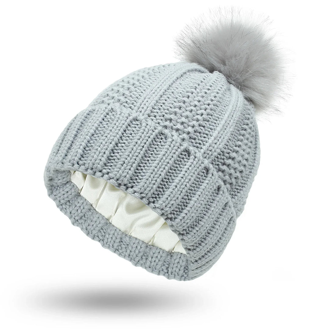 Light gray knitted winter beanie hat with faux fur pompom and satin lining