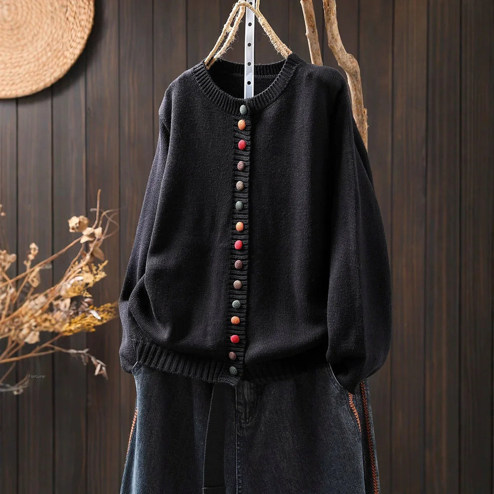 Black knitted cardigan with colorful buttons hanging on rustic wooden background with dried flowers