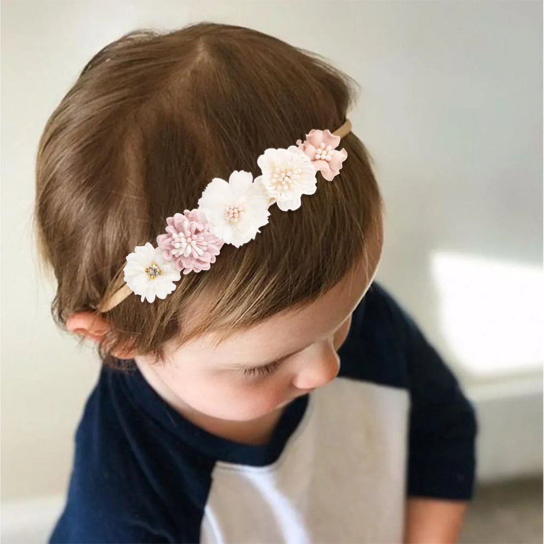 Toddler wearing beige flower headband with white and pink blossoms, navy and white shirt, indoor light