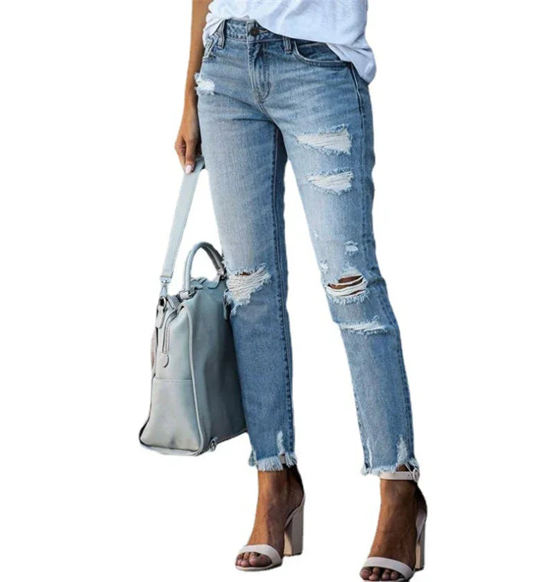 Woman wearing light blue ripped skinny jeans with frayed hems, white top, beige high heel sandals, and carrying gray handbag