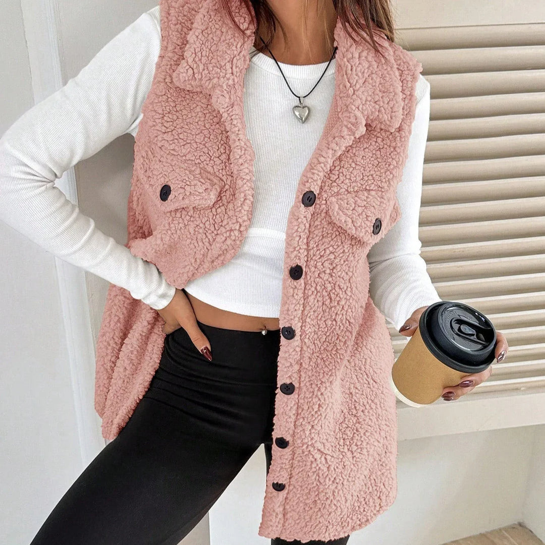 Woman wearing pink button-up sherpa vest, white long sleeve crop top, black leggings, holding coffee cup