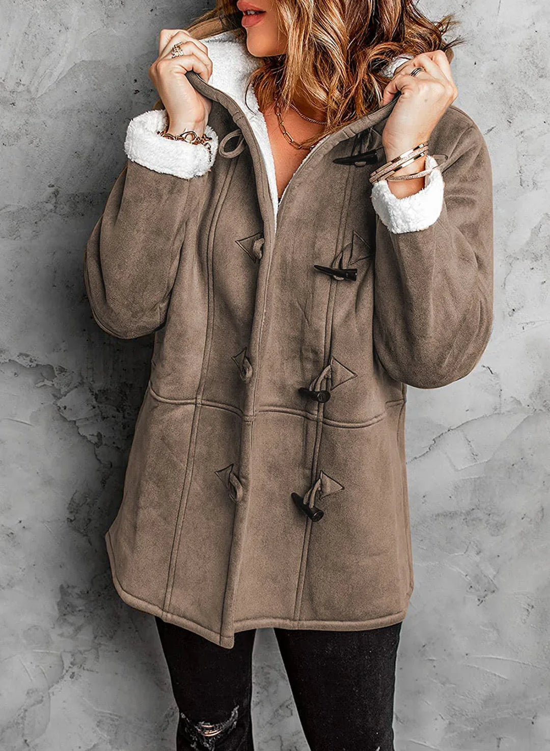 Woman wearing a brown faux suede toggle coat with white sherpa lining and black ripped jeans