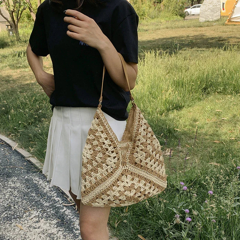 Woman in black shirt and white pleated skirt holding a large handmade crochet tote bag outdoors