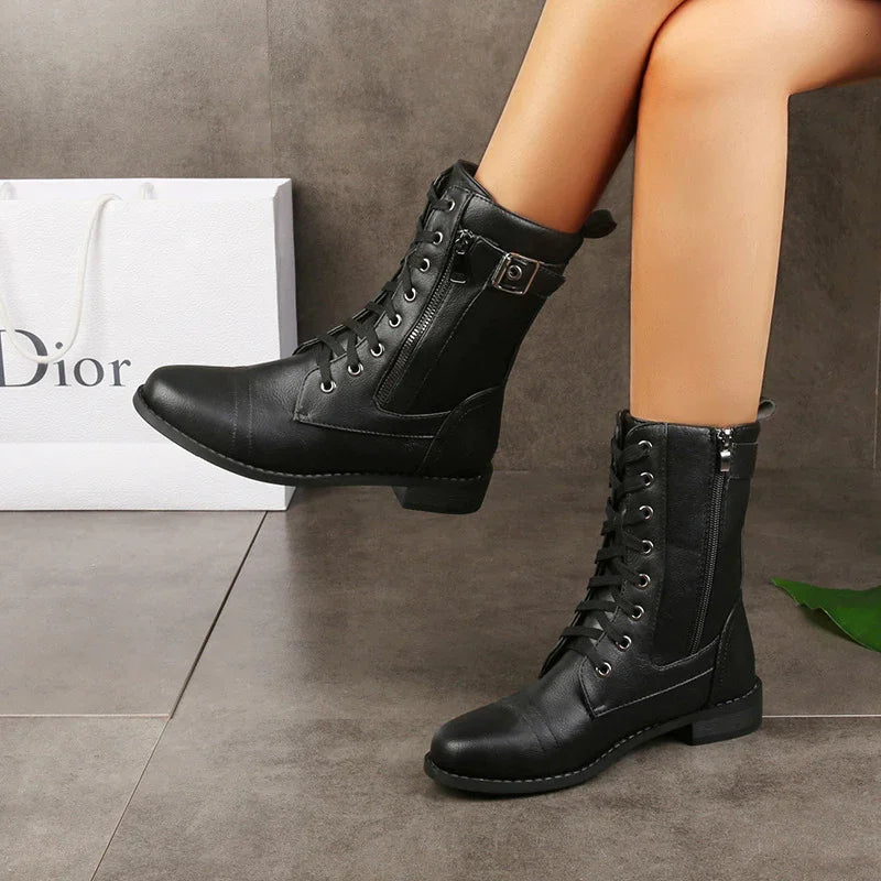 Black leather mid-calf lace-up boots with zipper and buckle detail worn on light-skinned legs on tile floor