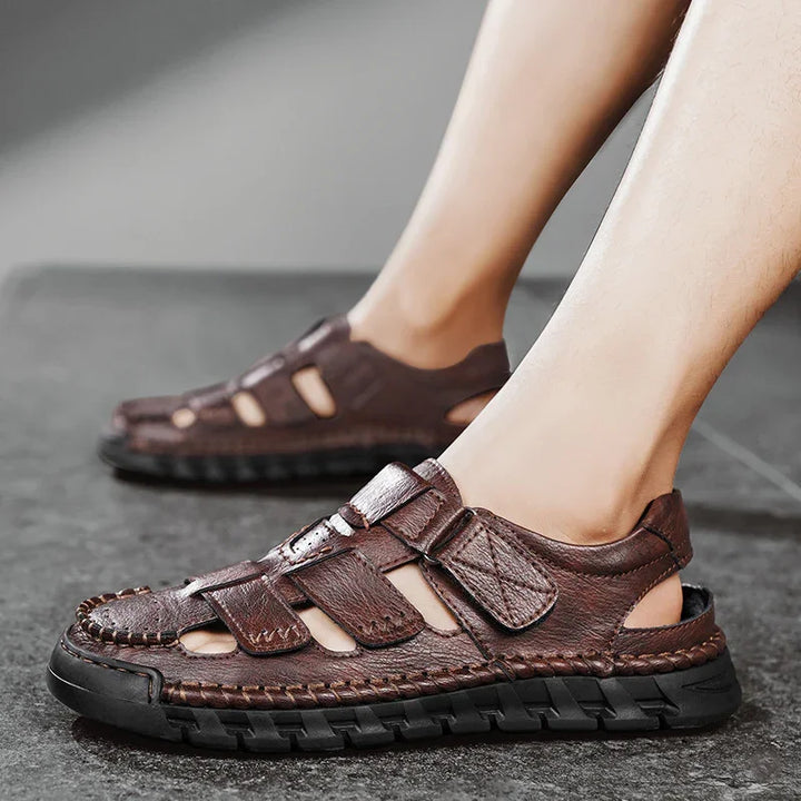 Men's brown leather casual sandals with black rubber soles worn indoors on gray floor