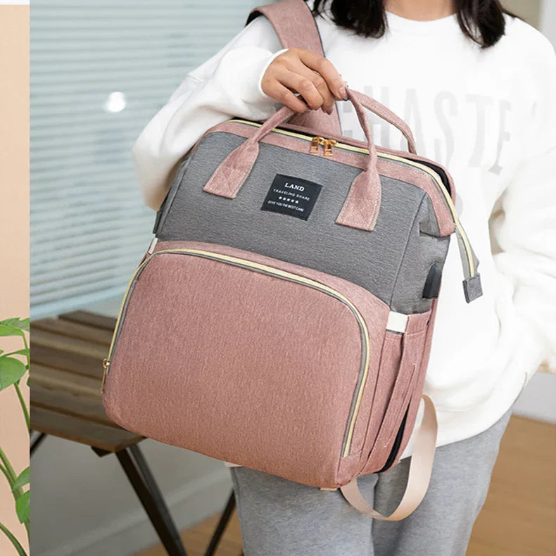 Woman holding pink and gray travel backpack with multiple compartments and gold zippers