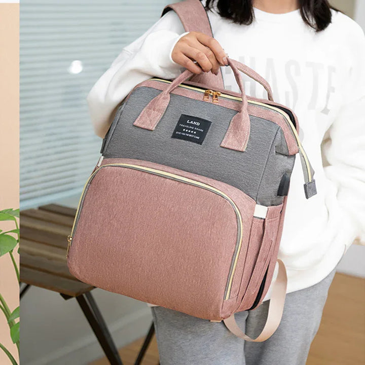 Woman holding pink and gray travel backpack with multiple compartments and gold zippers
