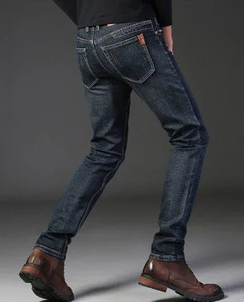 Rear view of person wearing dark blue slim-fit denim jeans and brown leather boots on grey background