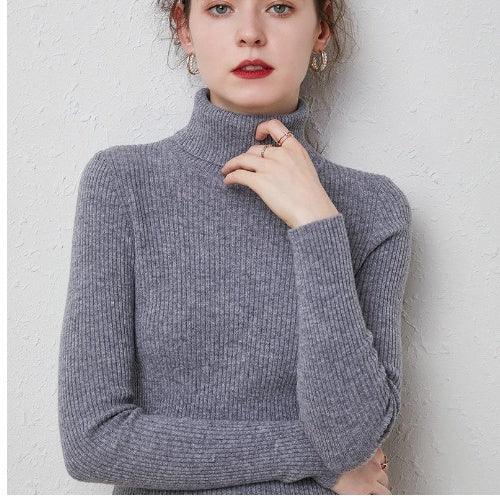 Young woman wearing a cozy gray ribbed turtleneck sweater against a light textured wall