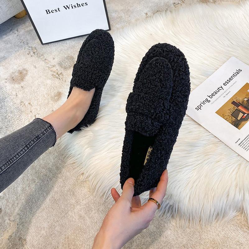 Cozy black textured slip-on loafers worn indoors on beige carpet with decor and magazine