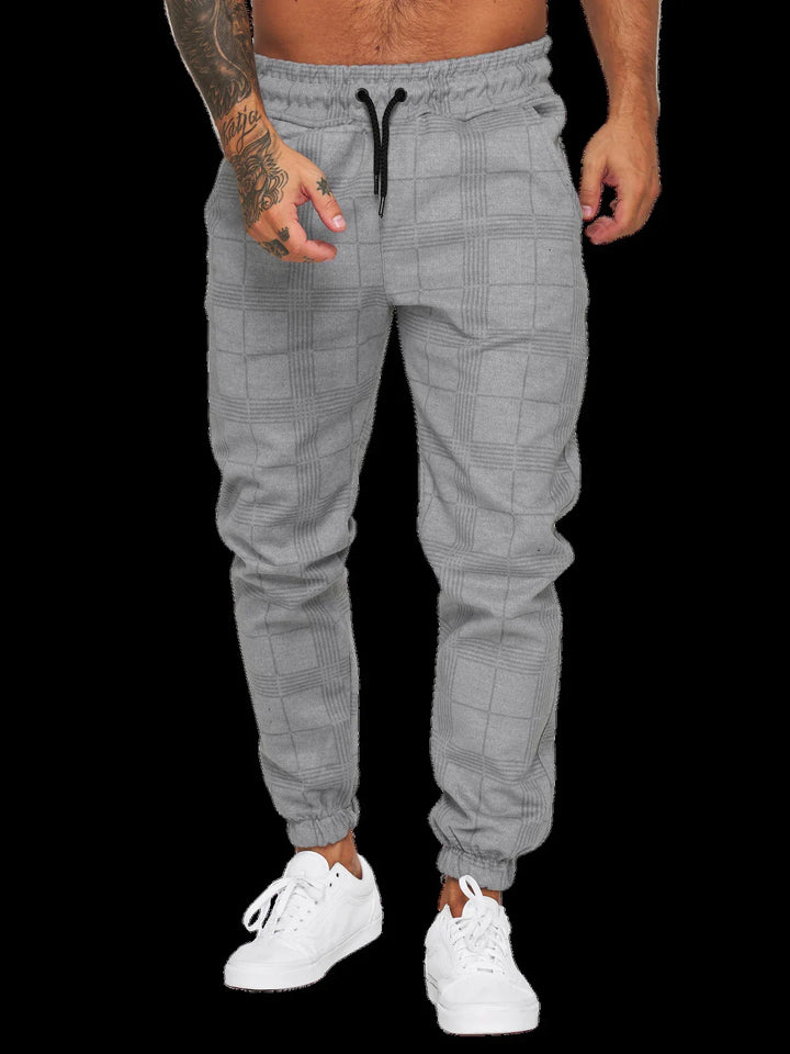 Man wearing light gray plaid jogger pants with black drawstrings and white sneakers