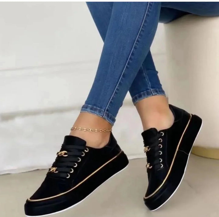 Close-up of black platform sneakers with gold chain accents and gold trim worn with blue skinny jeans