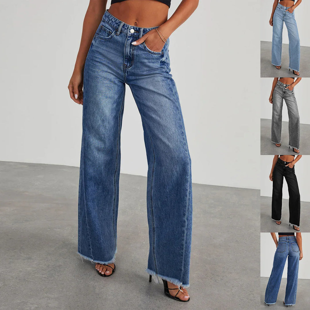 woman wearing high-waisted wide-leg blue denim jeans with raw hem and black strappy heels on gray floor