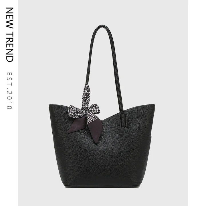 Black leather tote bag with long handles and black-and-white patterned bow accessory on handle